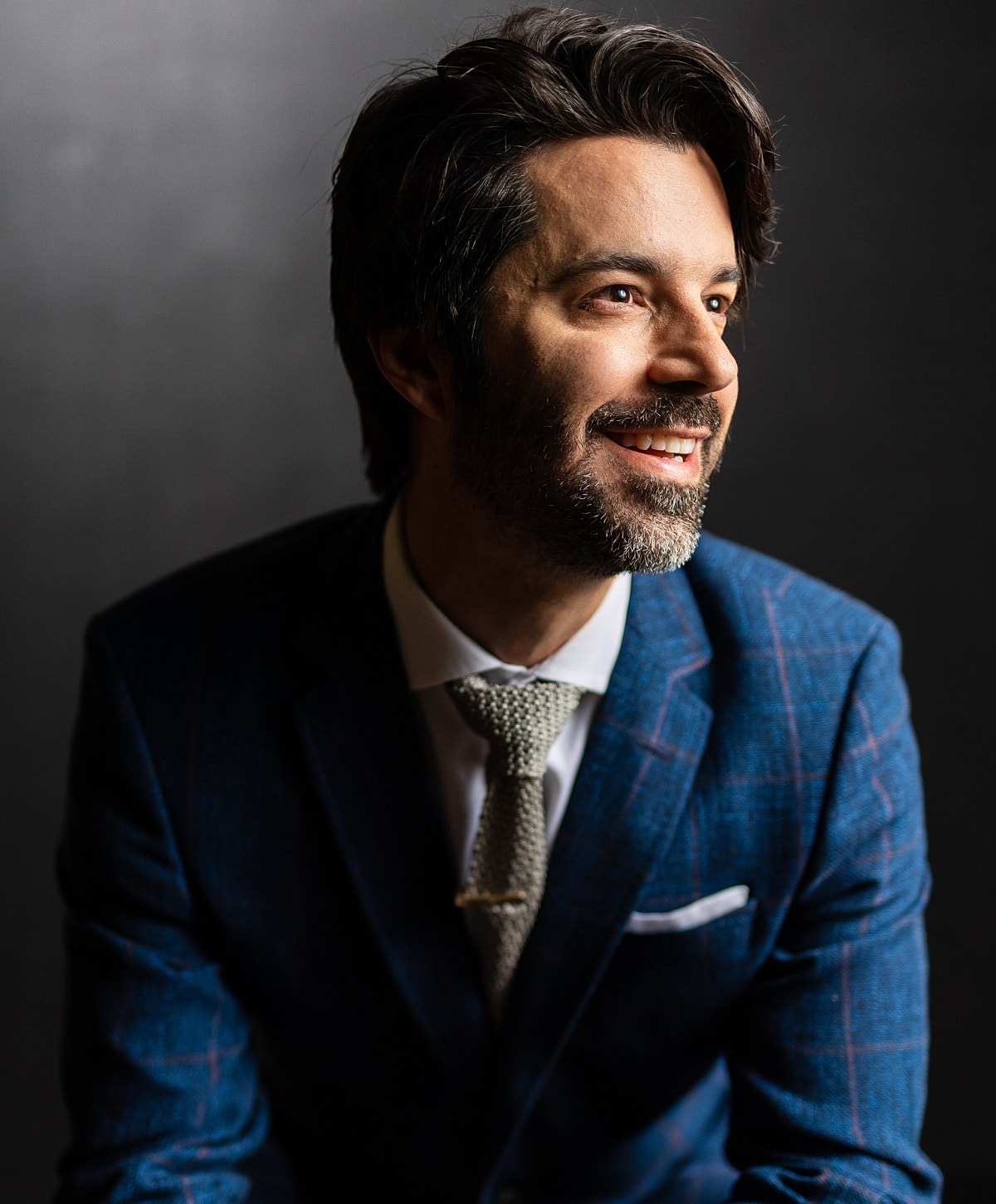 Man smiling in a suit against a dark background.
