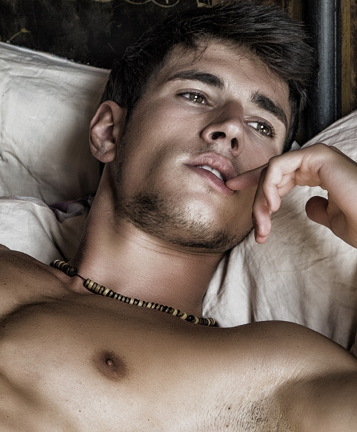 Young man lounging on bed, thoughtful expression.