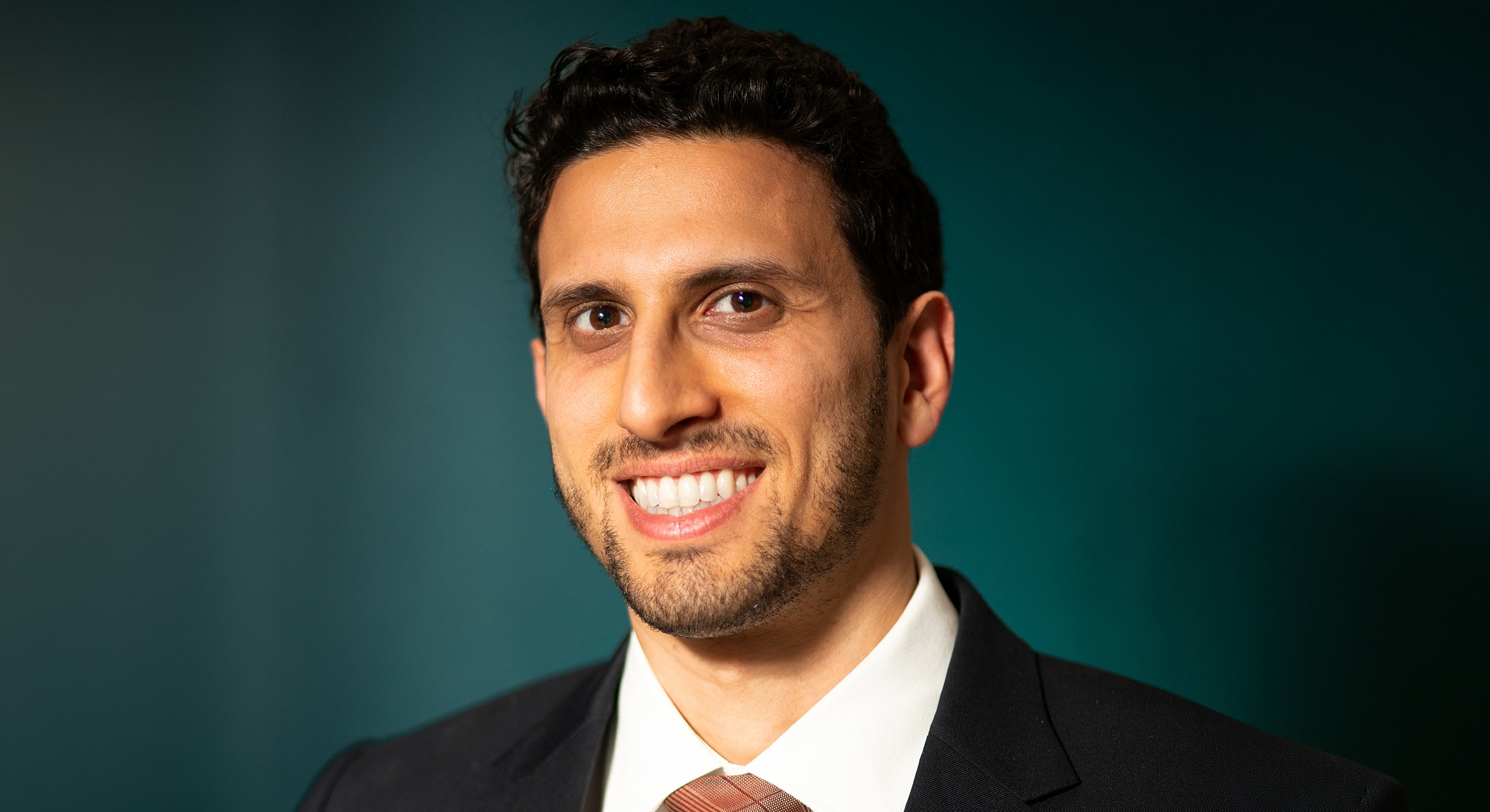 Smiling man in a suit against dark background.